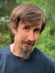 John Darnielle of Mountain Goats in a portrait outside with green leaves in background